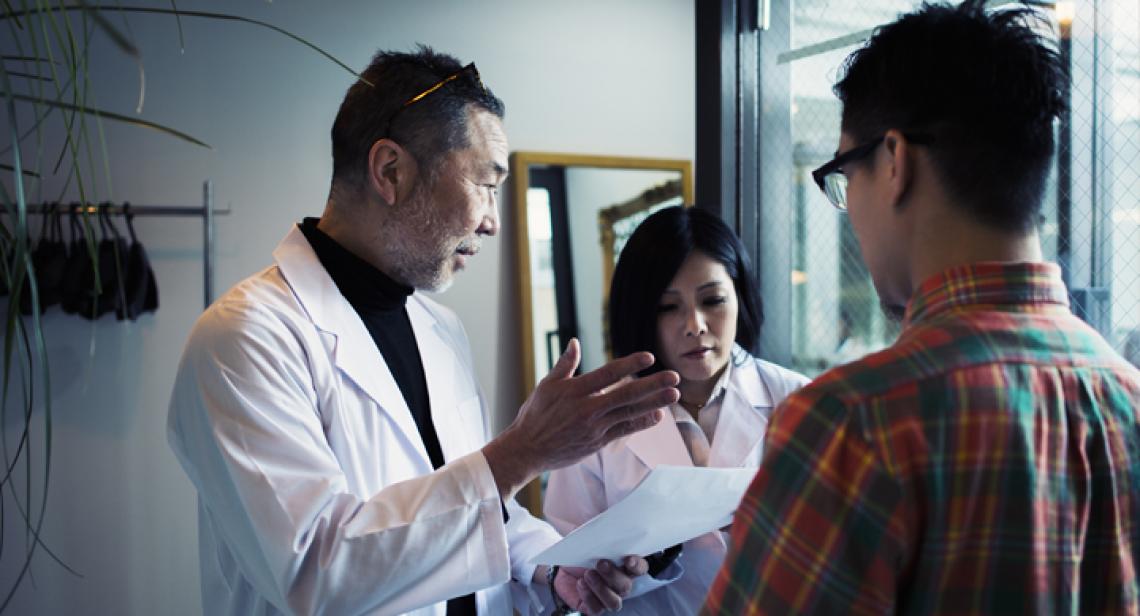 doctor giving notes to intern in front of patient